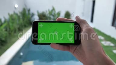 智能手机的特写与绿色屏幕坐在靠近游泳池的家中，由人保持水平模式，<strong>看电影</strong>